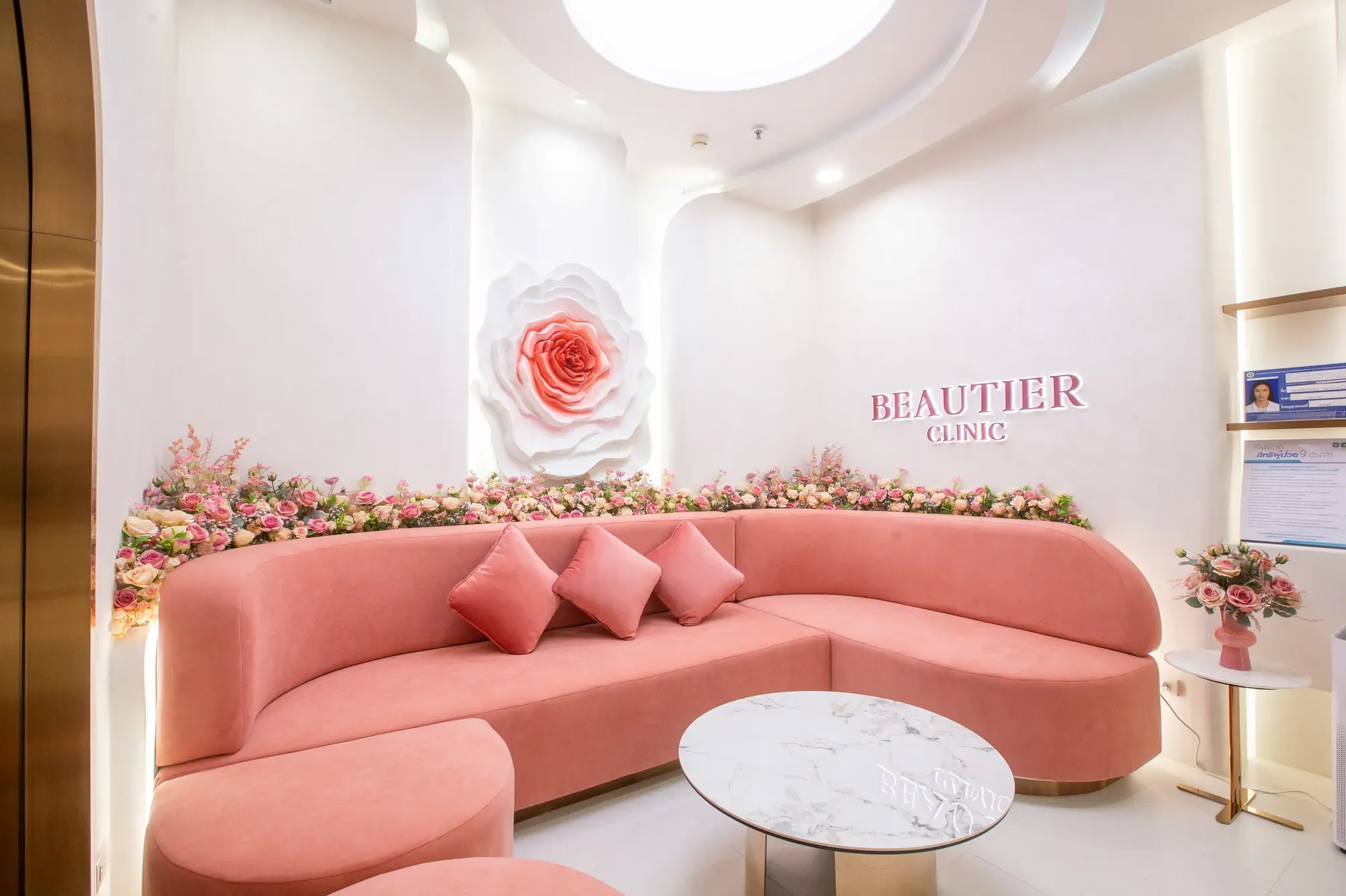 โซฟาสีชมพูและผนังดอกไม้ในพื้นที่รับรอง Beautier Clinic